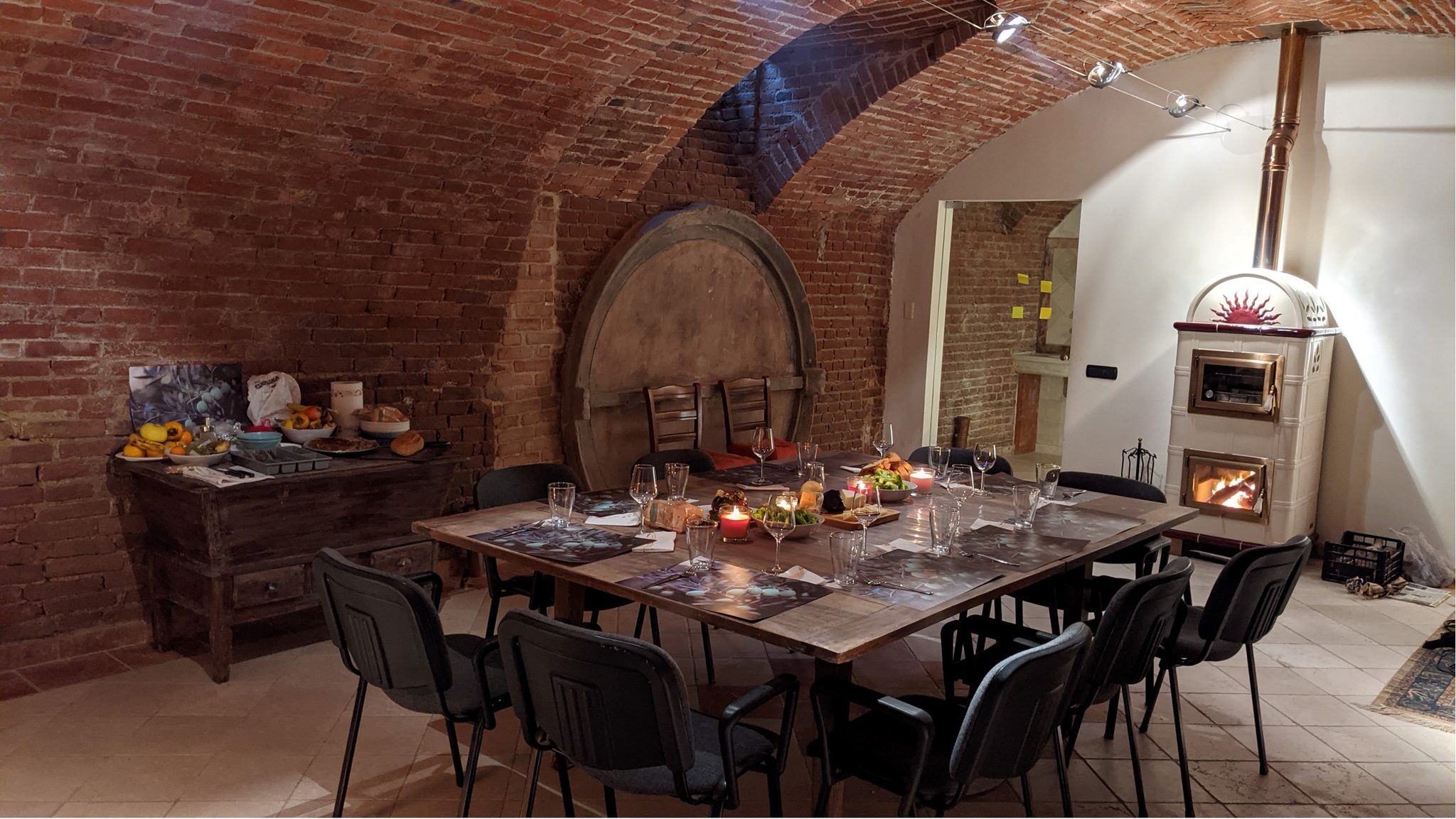 The brick barrel-vaulted cantina laid for dinner: a long wooden table set with glasses and candles beside a wood-fired stove